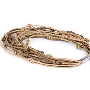 May include: A multi-strand necklace with knotted cords in beige, olive green, and brown hues. The necklace has a magnetic clasp. The accessory is displayed on a white background. This necklace is suitable for everyday wear.