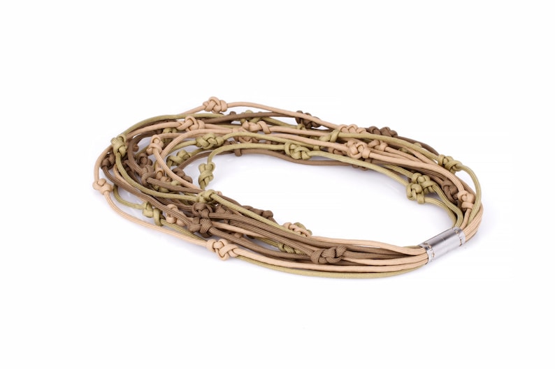 May include: A multi-strand necklace with knotted cords in beige, olive green, and brown hues. The necklace has a magnetic clasp. The accessory is displayed on a white background. This necklace is suitable for everyday wear.