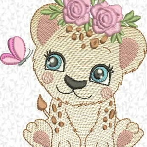 Pode incluir: Um design de bordado de um filhote de leão sentado com pelo castanho claro e manchas castanhas. O filhote tem olhos grandes azuis, orelhas cor-de-rosa por dentro e uma coroa de rosas cor-de-rosa com folhas verdes e uma pequena borboleta.