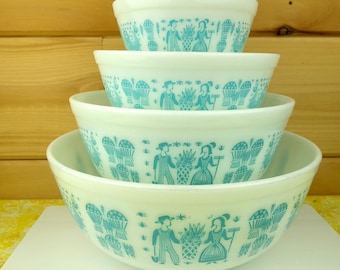 May include: Set of four white mixing bowls with a blue and white folk art pattern. The bowls are stacked in order of size, with the largest bowl on the bottom and the smallest bowl on top.