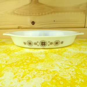 May include: White divided casserole dish with a brown floral pattern. The dish has a rounded oval shape with a lip around the edge.