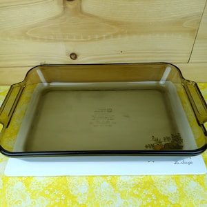 May include: A brown glass baking dish with a white interior. The dish is sitting on a white and yellow patterned surface.