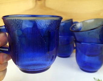 May include: Set of four cobalt blue glass cups with a ribbed design. The cups have a rounded shape and a small handle.