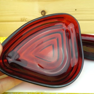 May include: A set of two red glass dishes with a concentric circle design. The dishes are shaped like a triangle with rounded edges.