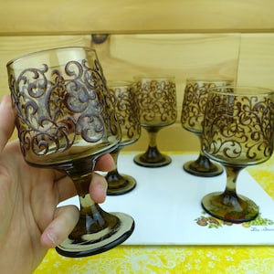 May include: Set of five brown glass wine glasses with a swirling black design. The glasses have a stemmed base.