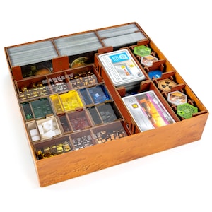 May include: A wooden game organiser with compartments for storing game pieces, cards, and tokens. The organiser has a brown wood finish and is filled with various game components, including small cubes, tiles, and cards.