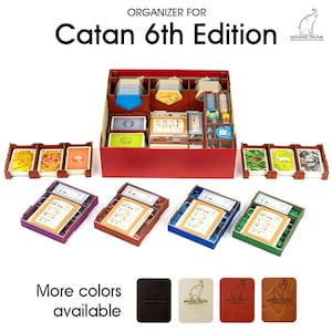 May include: A red wooden organizer for the Catan 6th Edition board game, with compartments for game pieces and cards. Includes four coloured player trays and card holders. Text reads "Organizer for Catan 6th Edition".