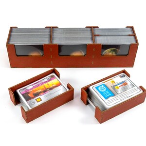 May include: A brown wooden organiser with three compartments for storing cards. The organiser has clear plastic windows to view the cards. Two smaller brown wooden trays are also shown, each holding a stack of cards.