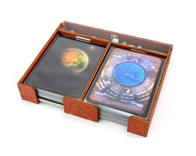 May include: A wooden box with two compartments for storing cards. The box is brown with a clear plastic lid. The box is filled with cards featuring images of planets and a control panel.