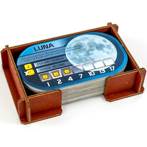 May include: A blue and white card game token with the word "LUNA" and a picture of the moon. The card has a colony bonus of 2 and a trade income of 2. The card also has numbers 1, 2, 4, 7, 10, 13, and 17.