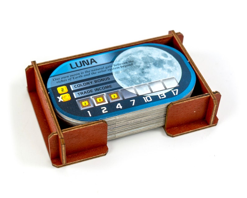 May include: A blue and white card game token with the word "LUNA" and a picture of the moon. The card has a colony bonus of 2 and a trade income of 2. The card also has numbers 1, 2, 4, 7, 10, 13, and 17.
