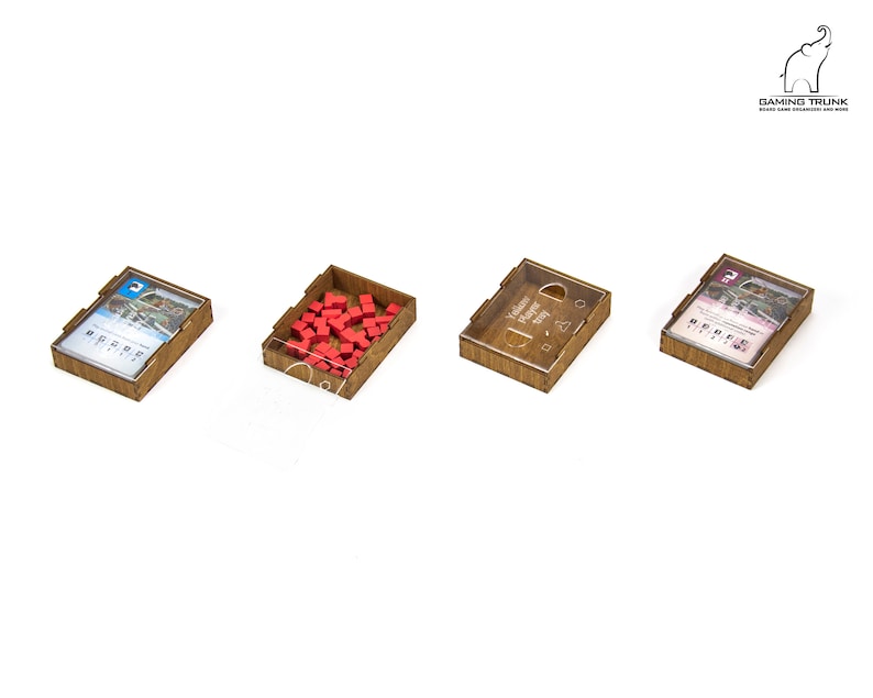 Pu&ograve; includere: Quattro scatole di legno con coperchi trasparenti, ciascuna contenente diversi componenti di gioco. Una scatola contiene cubi rossi, un'altra una carta con un'immagine di un ponte, e le altre due scatole contengono carte con testo.