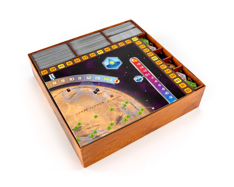 May include: A wooden game organiser with compartments for storing game pieces and cards. The organiser features a printed image of a planet with a hexagonal grid and the text "LUNAE PLANUM".