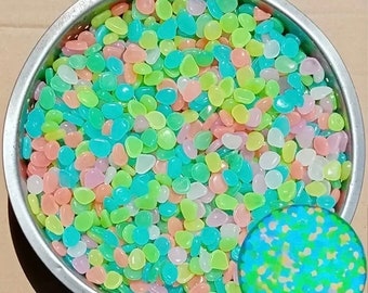 May include: A bowl filled with colorful glow-in-the-dark pebbles. The pebbles are a mix of light blue, green, pink, and white.
