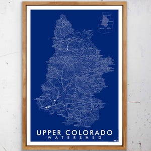 May include: A framed map of the Upper Colorado Watershed, featuring a detailed white illustration on a deep blue background. The map includes the text "UPPER COLORADO WATERSHED" in white. The frame is made of light brown wood.