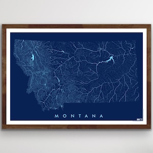 May include: A framed map of Montana, USA, with a detailed hydrographic design in shades of blue against a dark blue background. The word "MONTANA" is printed in white at the bottom. The frame is a dark brown color.