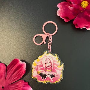 May include: Pink anime character keychain with long blonde hair and a pink and yellow outfit. The keychain is attached to a pink metal chain and a pink metal split ring.