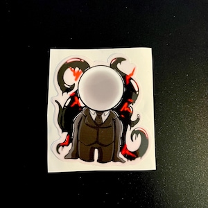 May include: A die-cut sticker featuring a character with a blank white circular head, wearing a dark brown suit with a tie. Behind the figure are black, tentacle-like shapes with bright red accents, all set against a white backing paper.