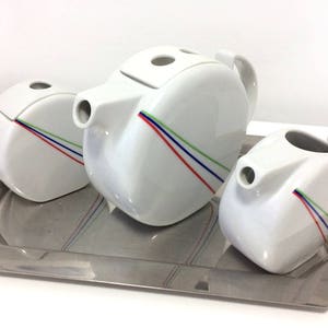 May include: A white porcelain teapot, creamer, and sugar bowl set with colourful stripes on a silver tray.