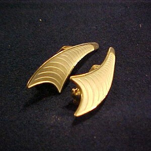 Peut inclure: Une paire de boucles d'oreilles dorées avec un motif géométrique blanc texturé. Les boucles d'oreilles ont la forme d'un croissant de lune.