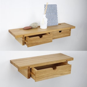 Puede incluir: Estante flotante de madera con cajón, mostrado en dos vistas. El estante es de madera clara y tiene forma rectangular. El cajón está abierto en una vista, revelando el interior. Un pequeño jarrón, papel decorativo y piedras están sobre el estante.