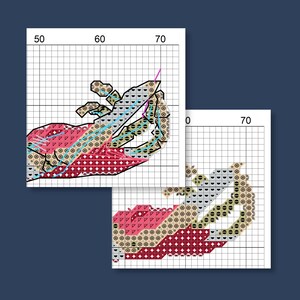 May include: Two cross-stitch patterns of a hand holding a needle and thread. The hand is depicted in shades of red, pink, tan, and blue, with a grid background. The needle is pink and the thread is purple.