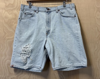 May include: Light blue denim shorts with a distressed look. The shorts have a faded appearance and a single hole on the left leg.