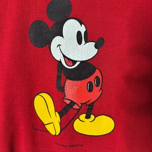 May include: Red sweatshirt with a Mickey Mouse graphic. The cartoon character is in black, white, red, and yellow. Mickey Mouse is shown walking with a smile. The text "&copy; WALT DISNEY PRODUCTIONS" is at the bottom of the image.