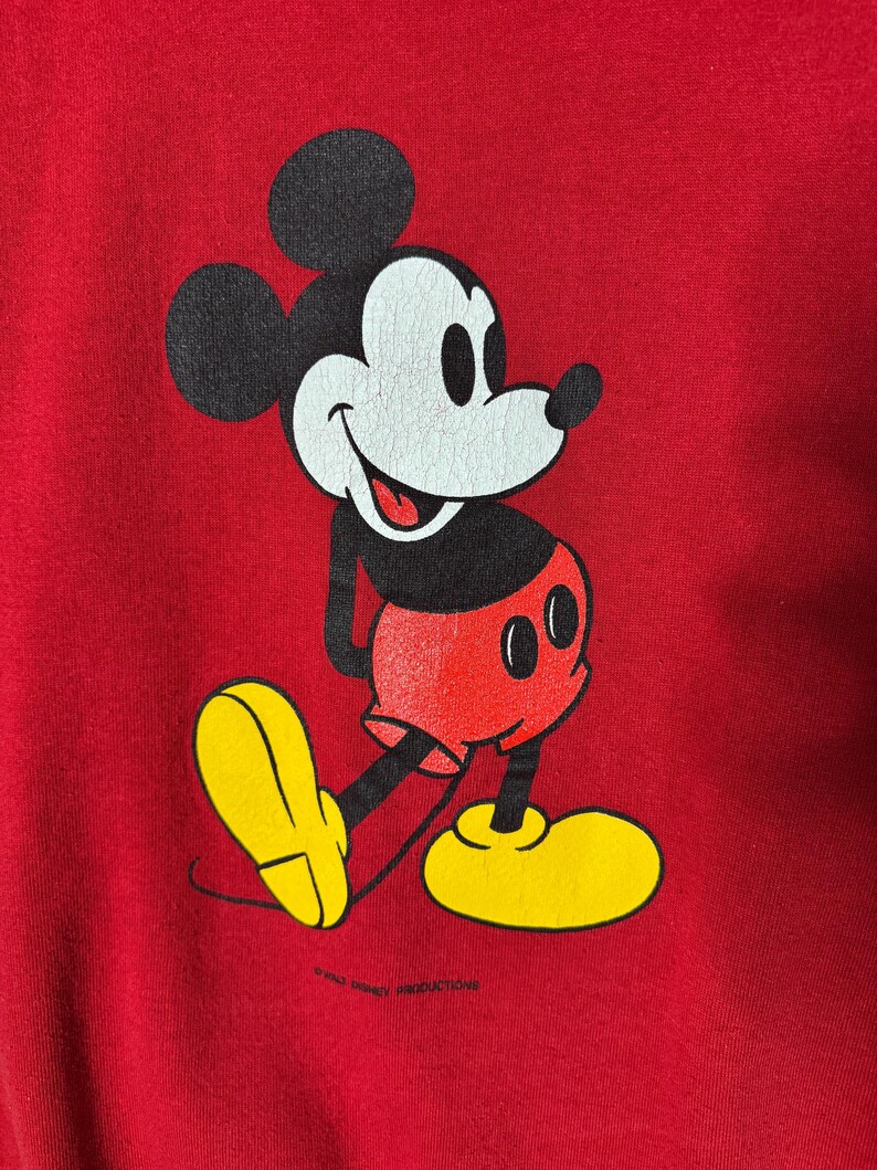 May include: Red sweatshirt with a Mickey Mouse graphic. The cartoon character is in black, white, red, and yellow. Mickey Mouse is shown walking with a smile. The text "&copy; WALT DISNEY PRODUCTIONS" is at the bottom of the image.
