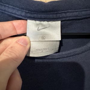 May include: Close-up of a navy blue t-shirt with a white tag. The tag features the Nike logo and the size XL. The tag also includes the text "MADE IN MEXICO".
