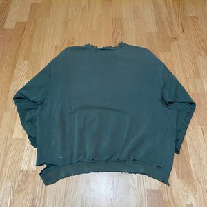 May include: A dark green sweatshirt with a distressed, worn look. The sweatshirt has a crew neck and long sleeves. The fabric has a soft, comfortable feel.