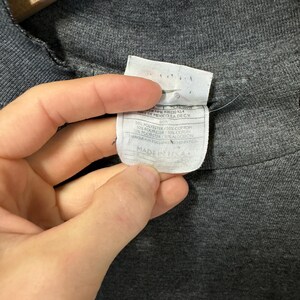 May include: A gray t-shirt with a white tag that reads "100% polyester / 50% cotton / 50% polyester / 50% cotton Made in Mexico, S.A. de C.V."