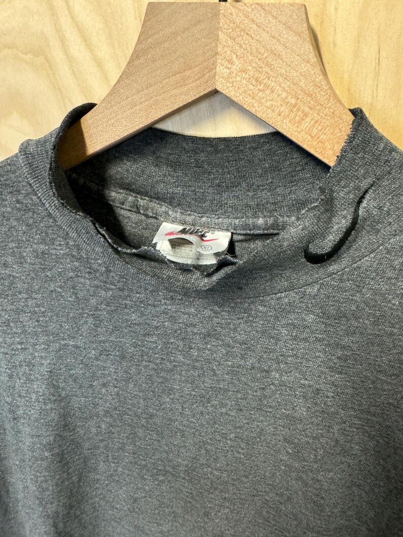 May include: A gray mock neck t-shirt with a Nike logo tag. The shirt is made of a soft, comfortable material.