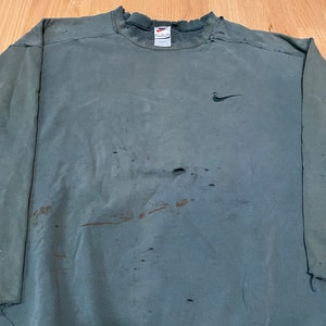 May include: A dark green sweatshirt with a Nike logo on the left chest. The sweatshirt has several holes and is distressed.