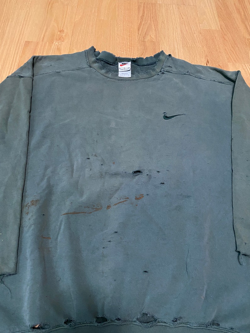 May include: A dark green sweatshirt with a Nike logo on the left chest. The sweatshirt has several holes and is distressed.