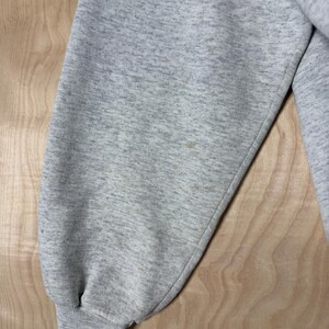 K&ouml;nnte beinhalten: Nahaufnahme eines hellgrauen Sweatshirt-&Auml;rmels. Der &Auml;rmel besteht aus einem weichen, strukturierten Stoff und hat ein geripptes B&uuml;ndchen. Auf dem &Auml;rmel befindet sich ein kleiner Fleck. Das Sweatshirt scheint Vintage oder gebraucht zu sein.
