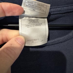May include: Close-up of a navy blue t-shirt with a tag attached. The tag includes text such as "100% COTTON" and "MADE IN MEXICO". The tag also includes the text "NIKE DE MEXICO, S.A. DE C.V."