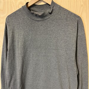 May include: A gray long-sleeved mock neck shirt hanging on a wooden hanger.