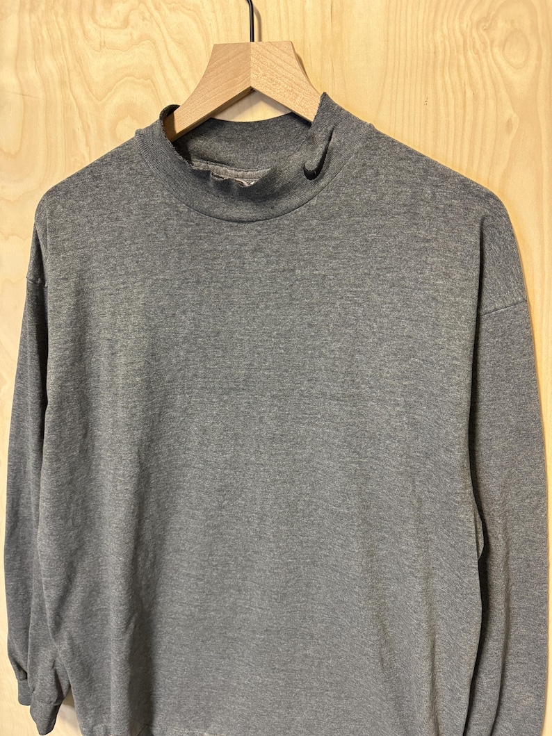 May include: A gray long-sleeved mock neck shirt hanging on a wooden hanger.