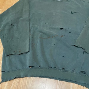 May include: A vintage green Nike sweatshirt with a small Nike logo on the chest. The sweatshirt has several holes and a frayed hem.