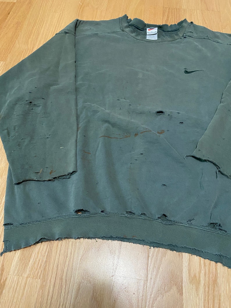 May include: A vintage green Nike sweatshirt with a small Nike logo on the chest. The sweatshirt has several holes and a frayed hem.