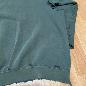 May include: A dark green sweatshirt with distressed edges and several small holes throughout.