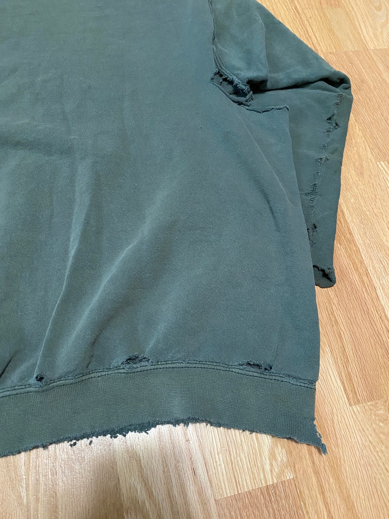 May include: A dark green sweatshirt with distressed edges and several small holes throughout.
