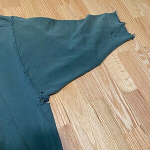 May include: A dark green long-sleeved shirt with several small holes in the fabric, particularly on the sleeve.