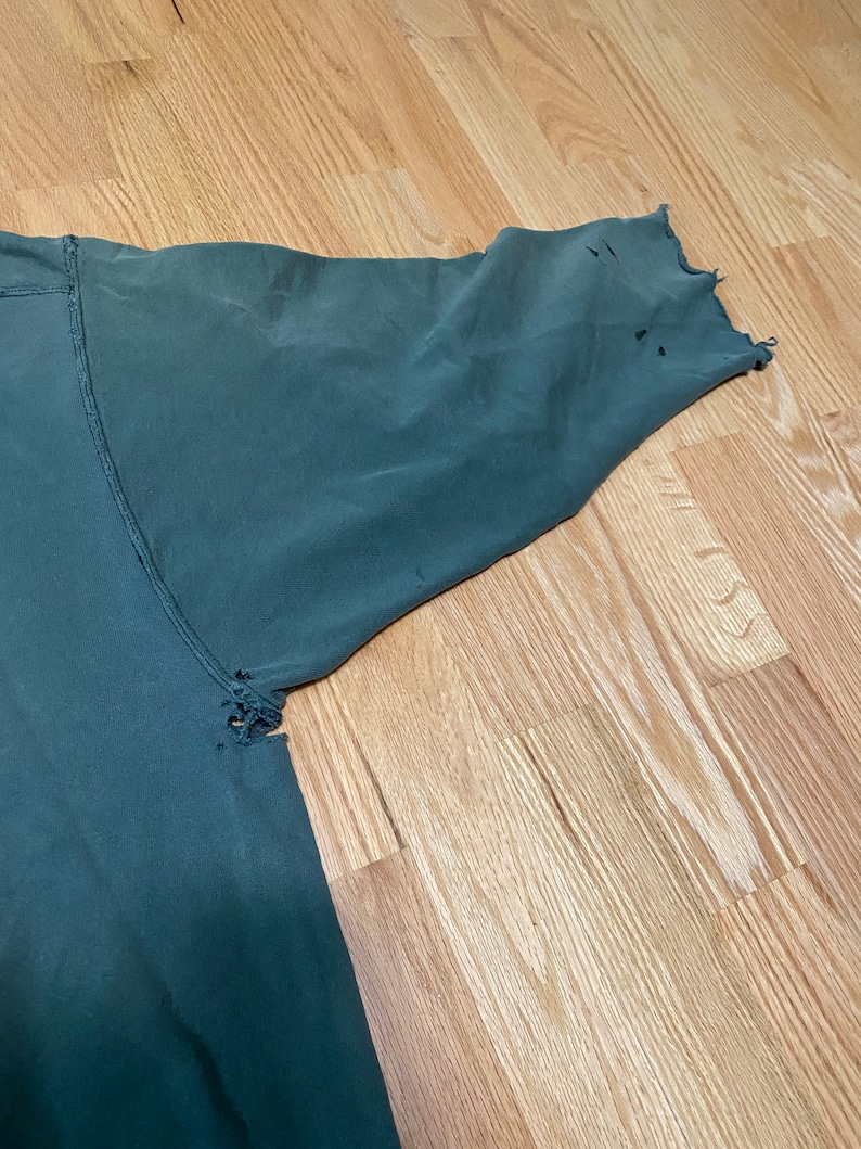 May include: A dark green long-sleeved shirt with several small holes in the fabric, particularly on the sleeve.