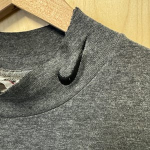 May include: Close-up of the neckline of a gray t-shirt with a black Nike swoosh logo.