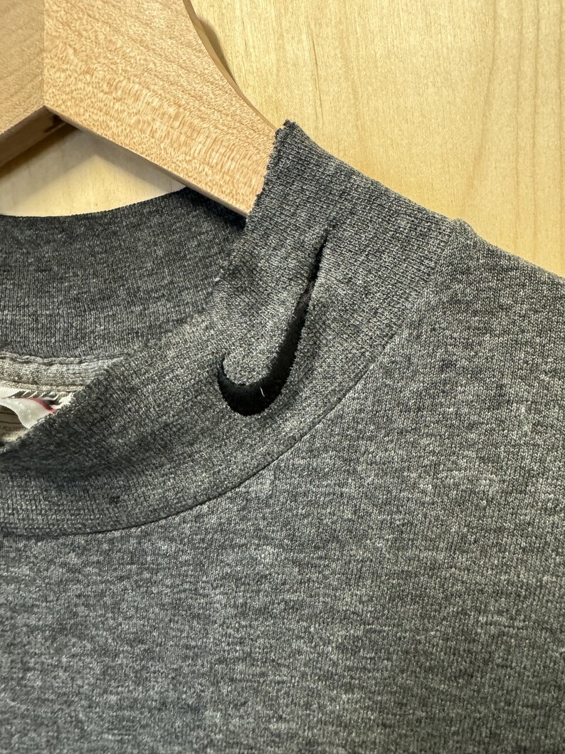 May include: Close-up of the neckline of a gray t-shirt with a black Nike swoosh logo.