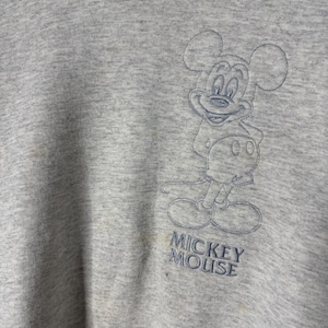 K&ouml;nnte beinhalten: Hellgraues Sweatshirt mit einem gestickten Bild von Mickey Mouse. Der Text "Mickey Mouse" ist unter der Figur gestickt. Das Sweatshirt hat einen Rundhalsausschnitt und lange &Auml;rmel.