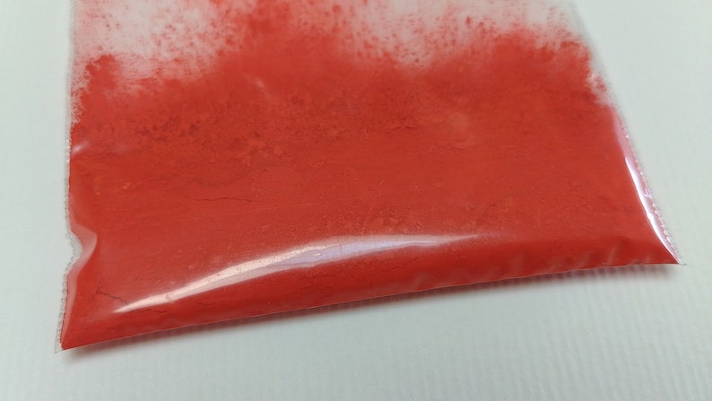 May include: A close-up of a small plastic bag filled with bright orange powder.