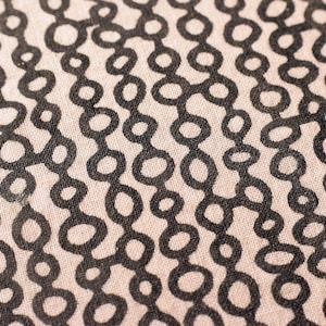 May include: Close-up of a fabric with a repeating pattern of connected black circles on a light beige background. The design creates vertical chains of linked shapes, offering a modern, abstract aesthetic. The fabric has a textured appearance.